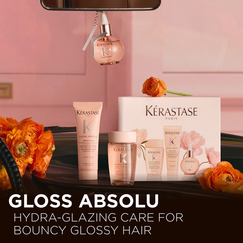 Kérastase Gloss Absolu Discovery Coffret and individual products displayed on a dark surface surrounded by orange ranunculus flowers with Hydra-Glazing Care for Bouncy Glossy Hair text overlay