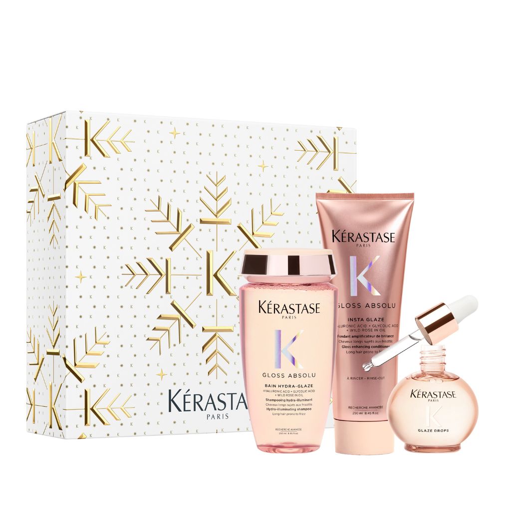 Kérastase Paris Gloss Absolu hair care gift set featuring a white box with gold snowflake patterns, a pink gloss bottle, a pink tube, and a round glass dropper bottle of Blac Saphir.